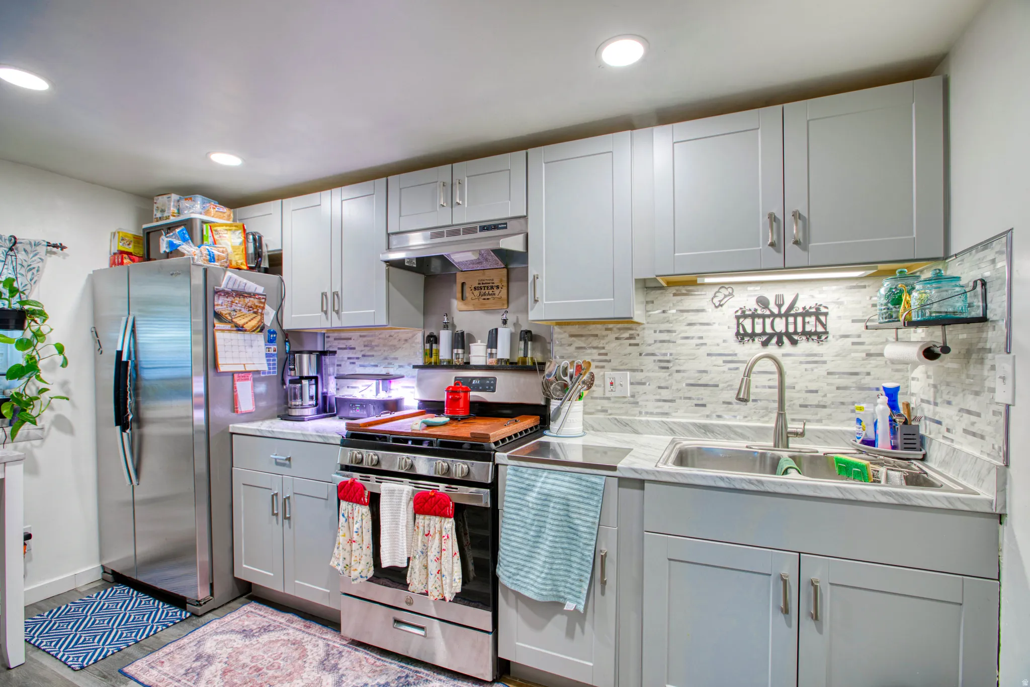 Kitchen with gray cabinets, stainless steel appliances, light countertops, backsplash, and dark wood-style flooring