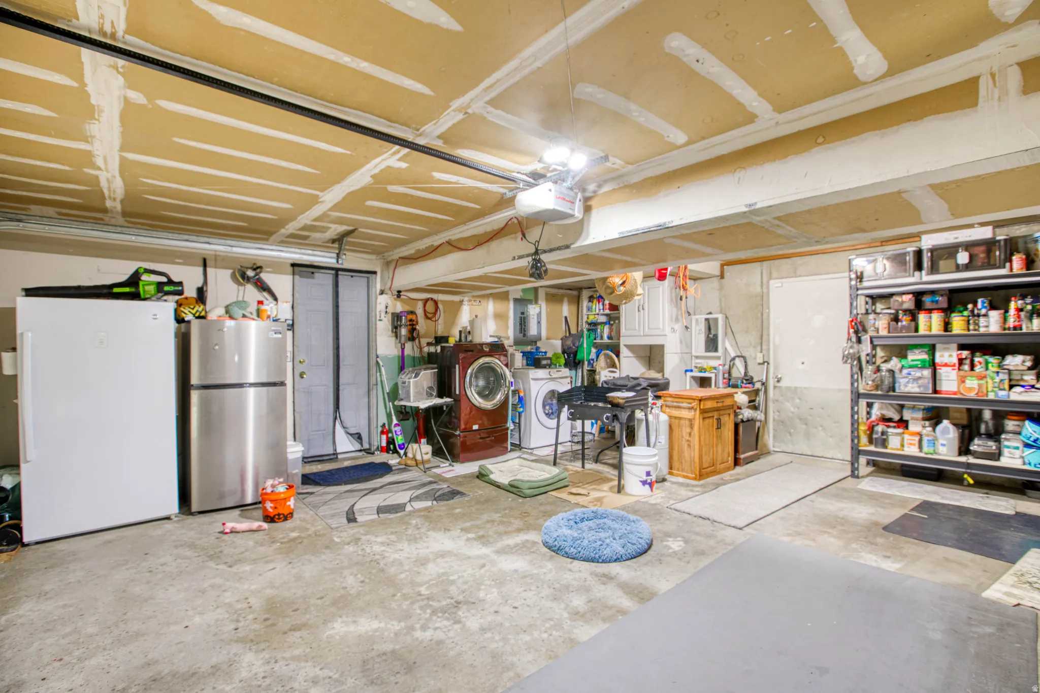 Garage with freestanding refrigerator, separate washer and dryer, a garage door opener, and electric panel