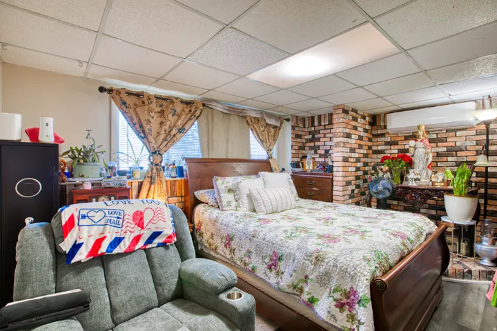 Bedroom with a paneled ceiling, brick wall, and wood finished floors