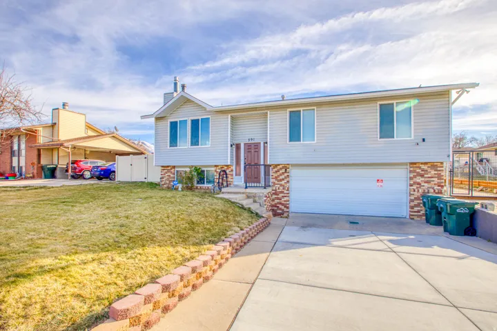 Raised ranch with brick siding, a garage, concrete driveway, and a gate