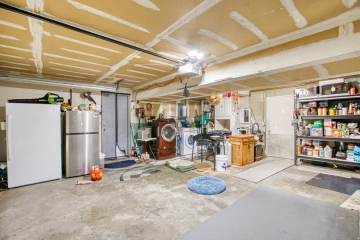 Garage with freestanding refrigerator, separate washer and dryer, a garage door opener, and electric panel