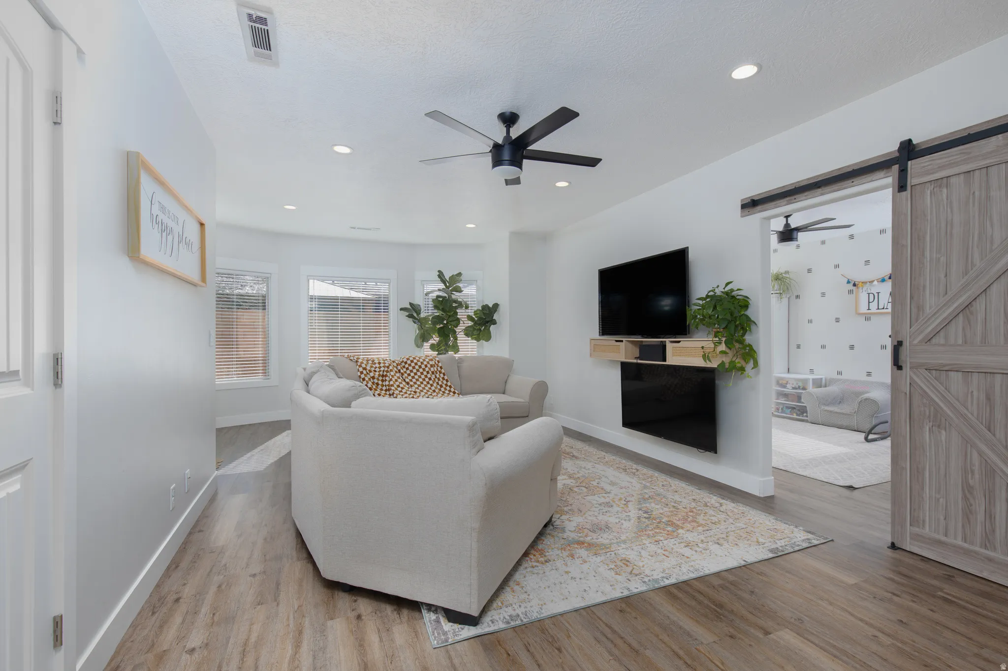 Living area featuring a barn door, a ceiling fan, light wood-type flooring, and recessed lighting