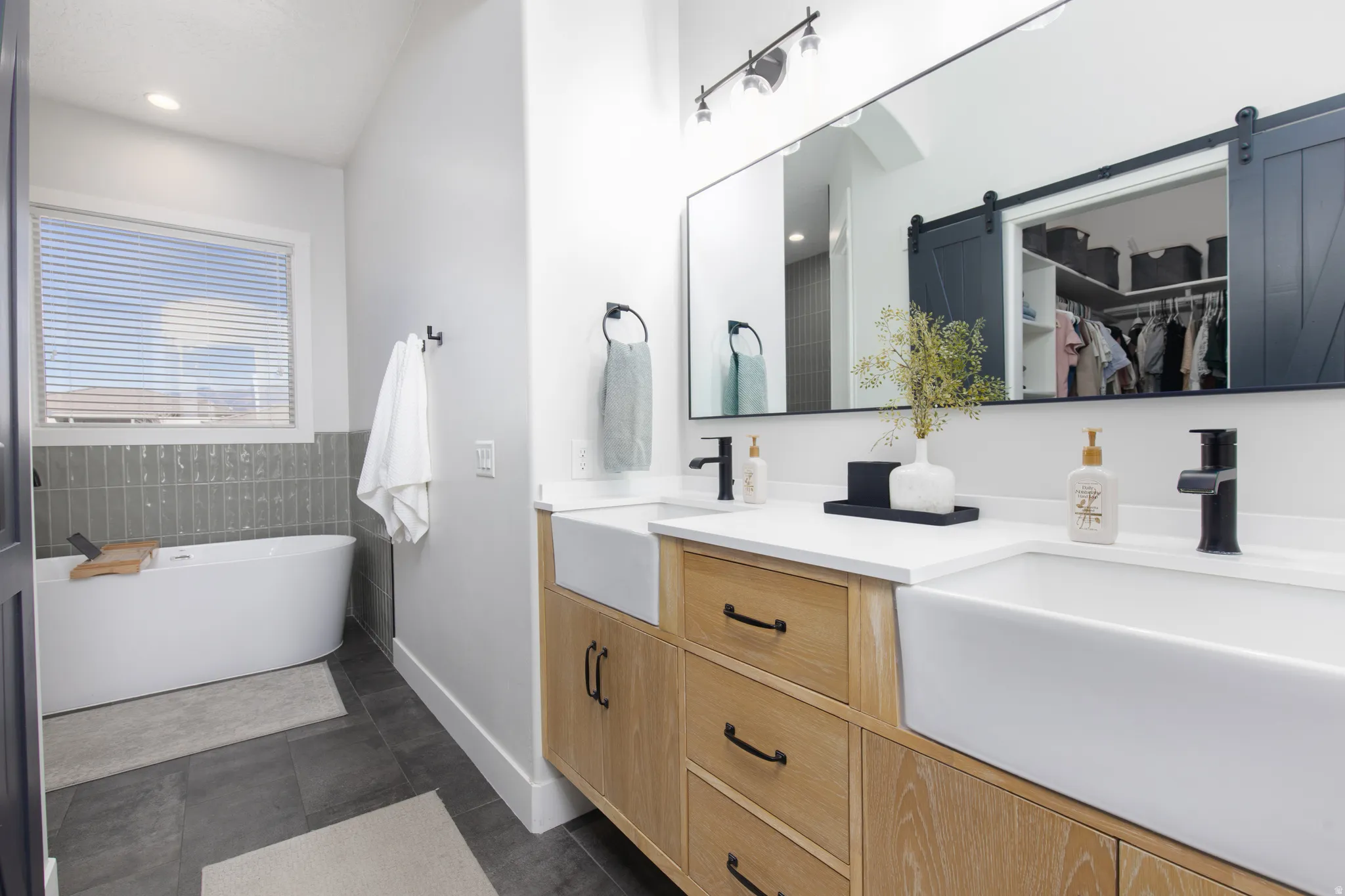 Bathroom with a spacious closet, a freestanding bath, double vanity, dark tile patterned flooring, and recessed lighting