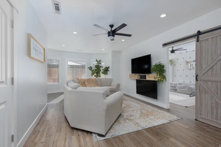 Living area featuring a barn door, a ceiling fan, light wood-type flooring, and recessed lighting