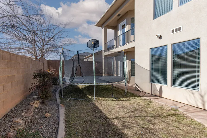 Fenced backyard with a trampoline and a balcony
