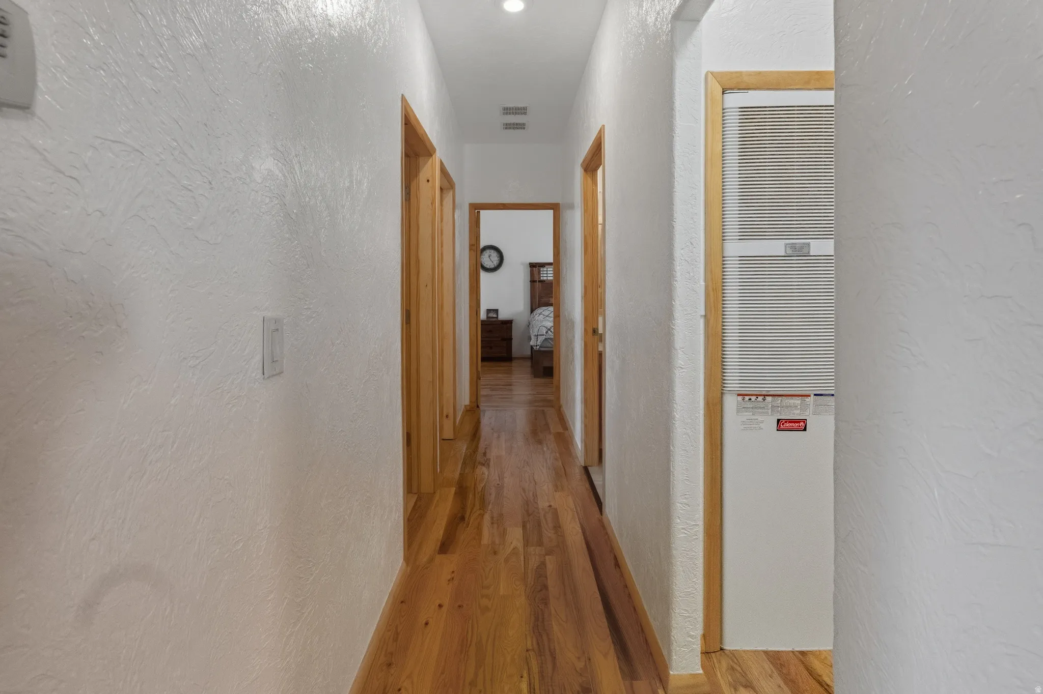Corridor featuring a textured wall, a heating unit, and light wood-type flooring