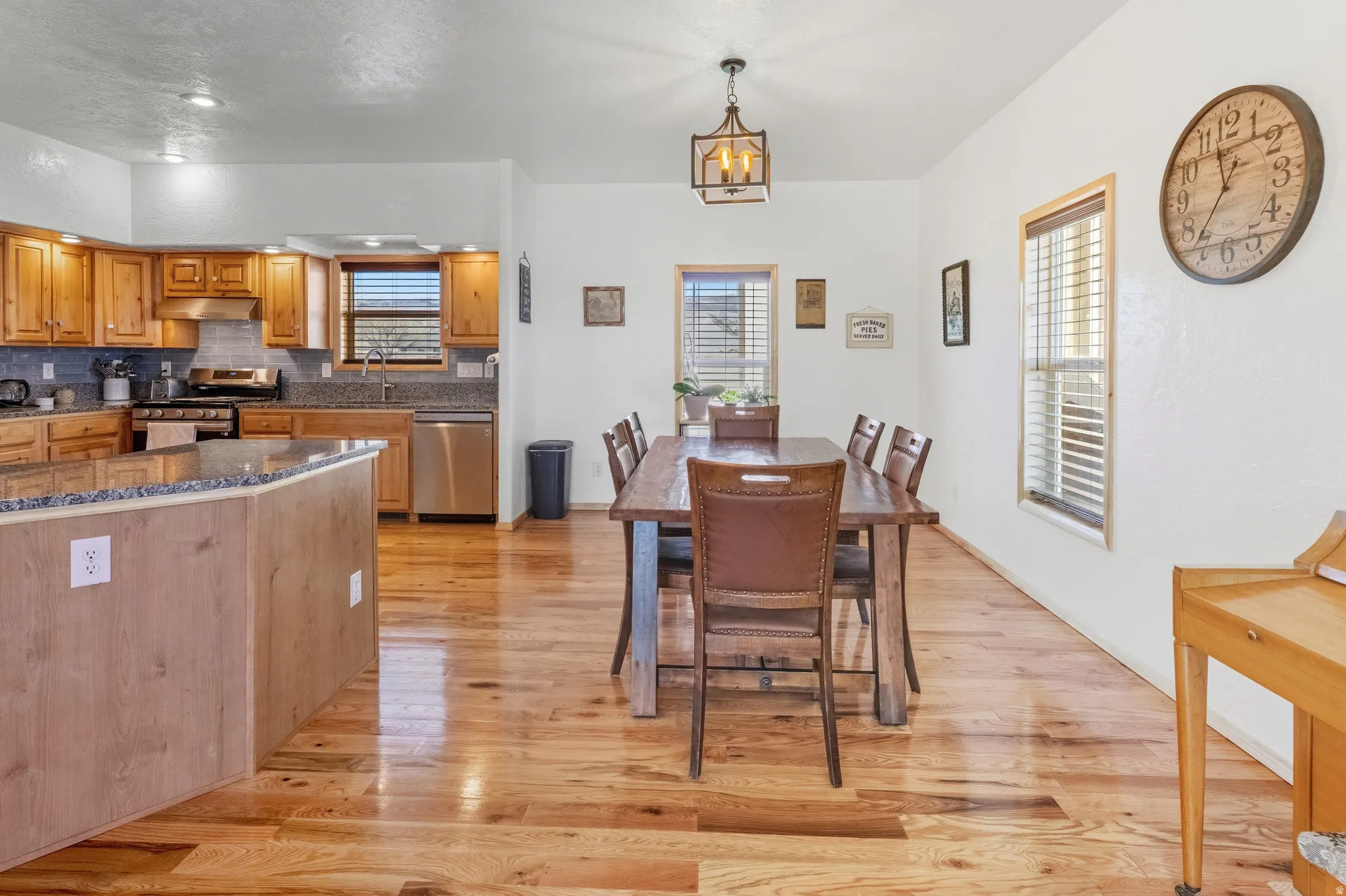 Kitchen with dark stone countertops, light wood-style floors, stainless steel appliances, and decorative light fixtures