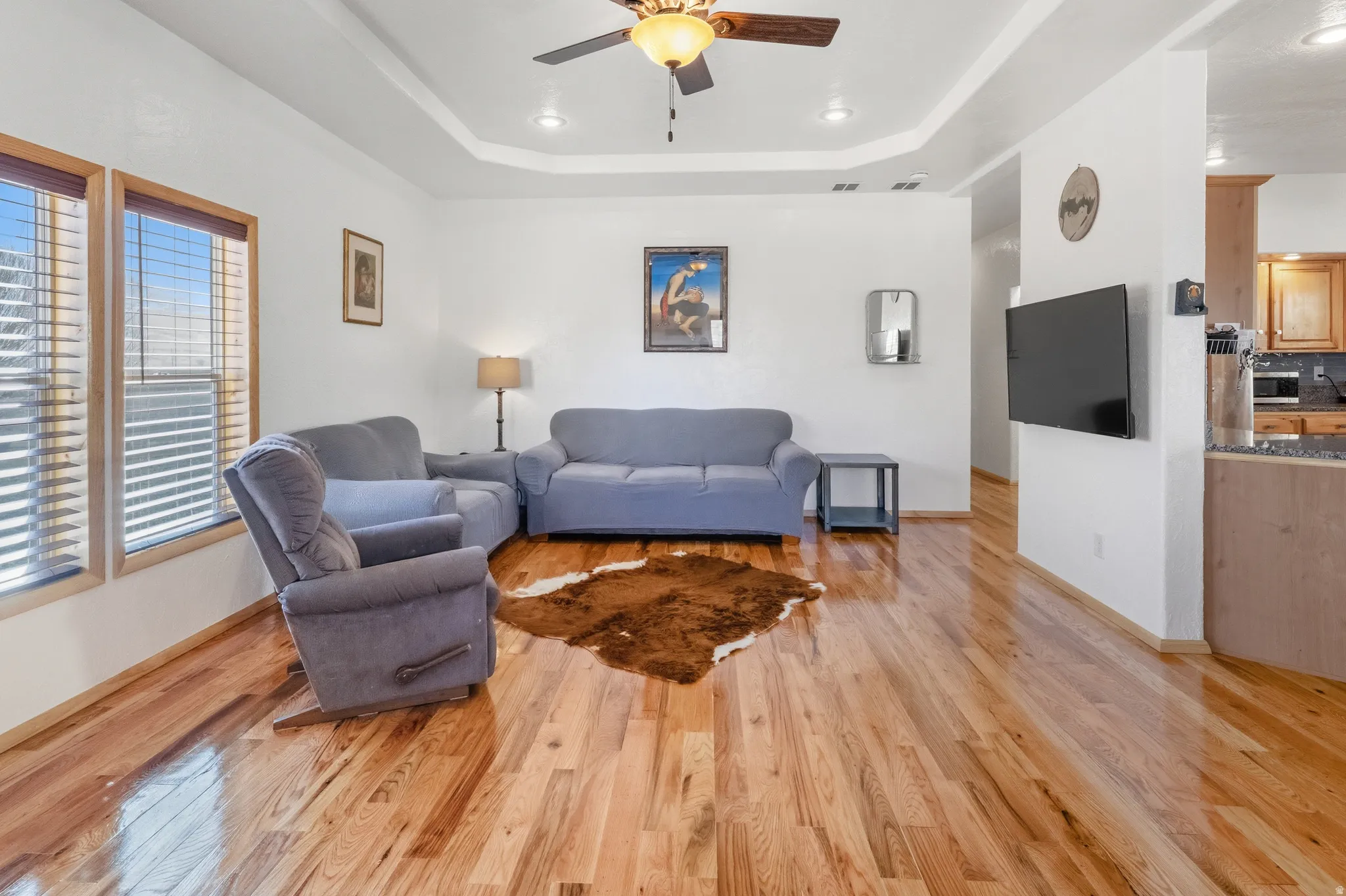 Living area featuring light wood-style floors, ceiling fan, a raised ceiling, and recessed lighting