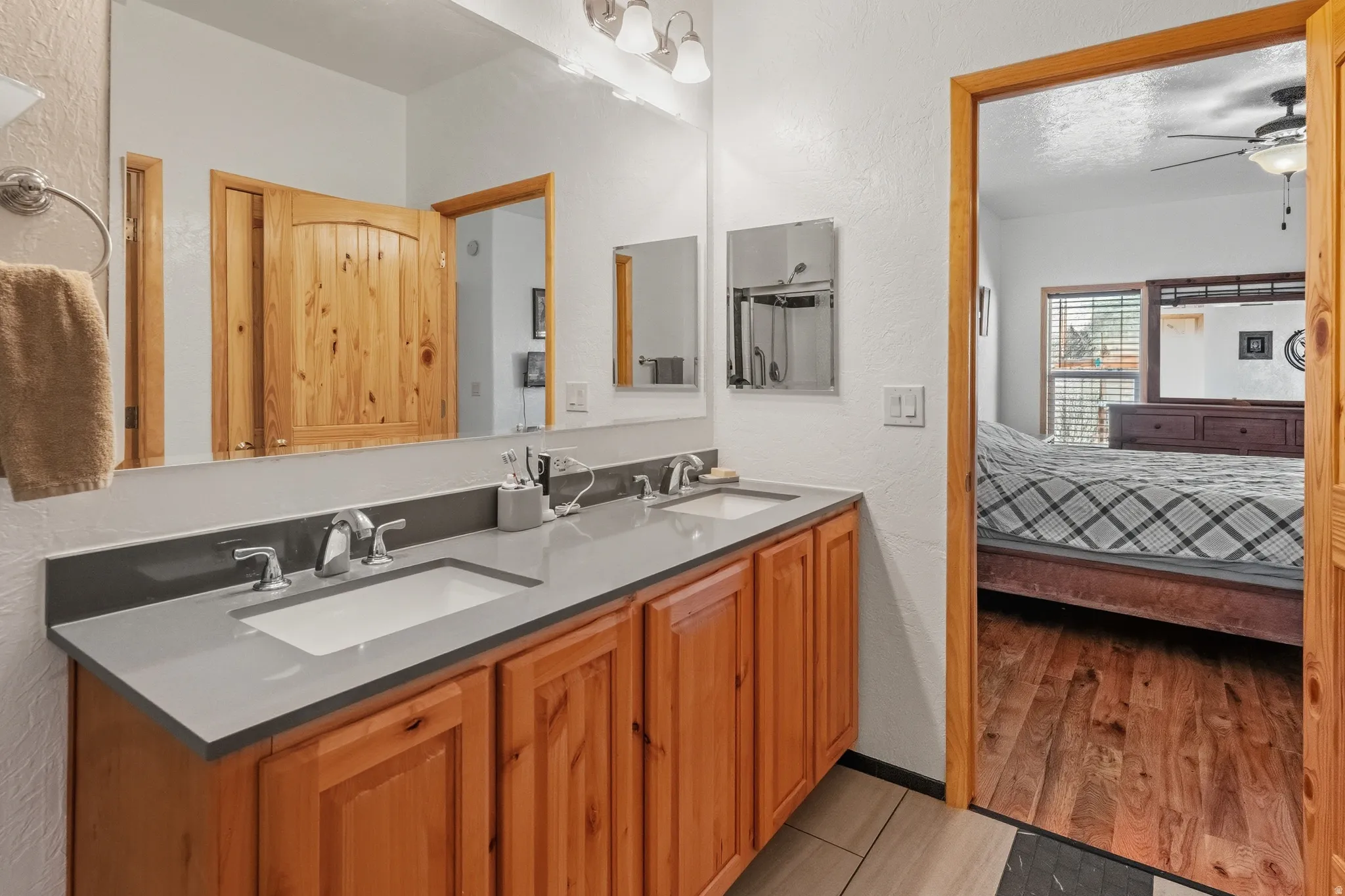 Full bathroom with a textured wall, connected bathroom, double vanity, ceiling fan, and light wood-style flooring