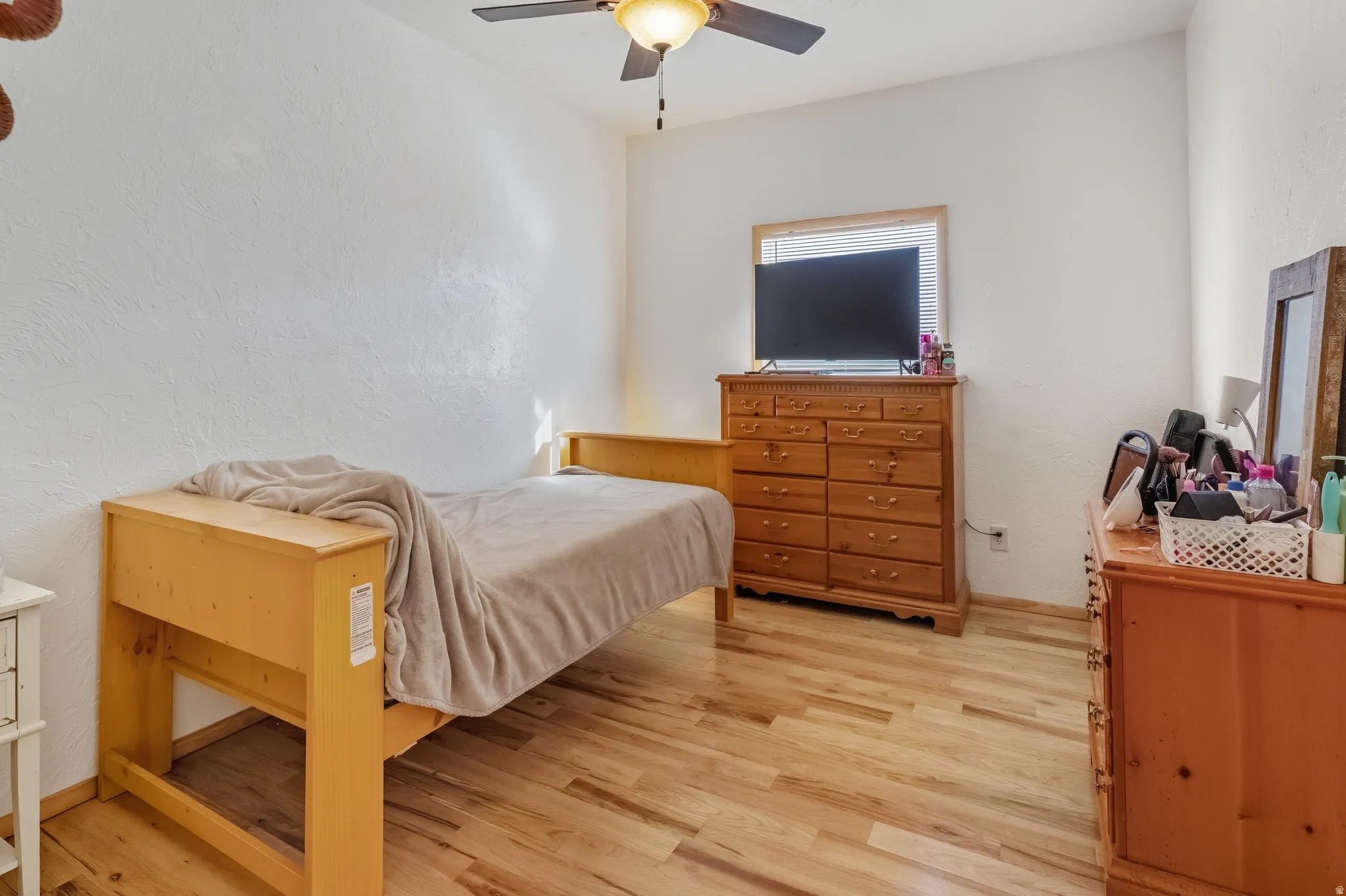Bedroom with light wood-style flooring, a textured wall, and ceiling fan