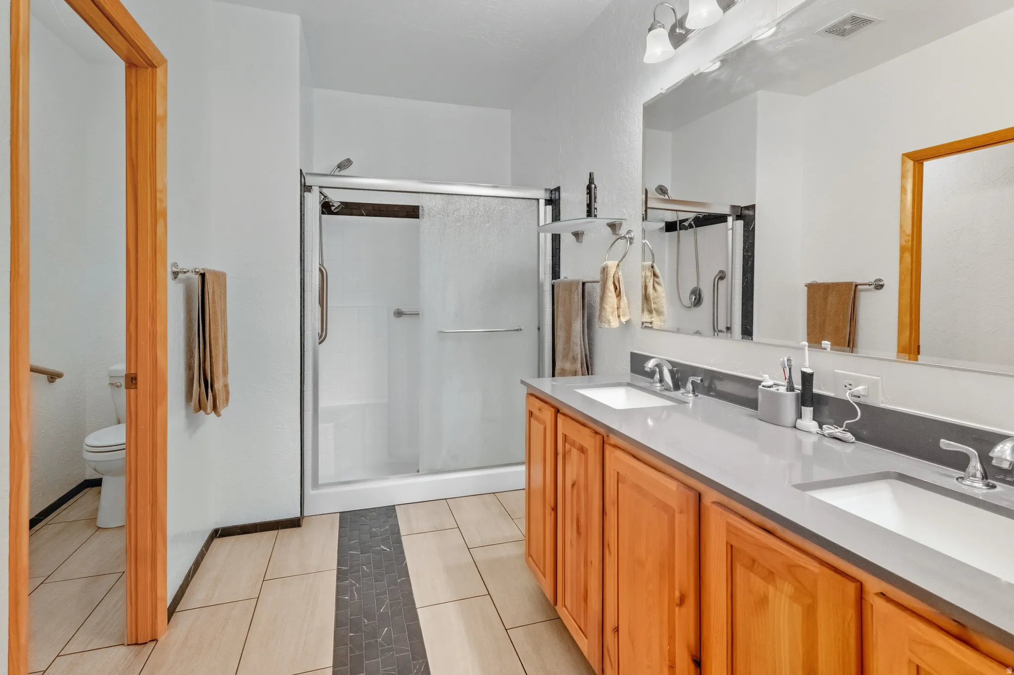 Bathroom with double vanity, a shower stall, and light tile patterned floors
