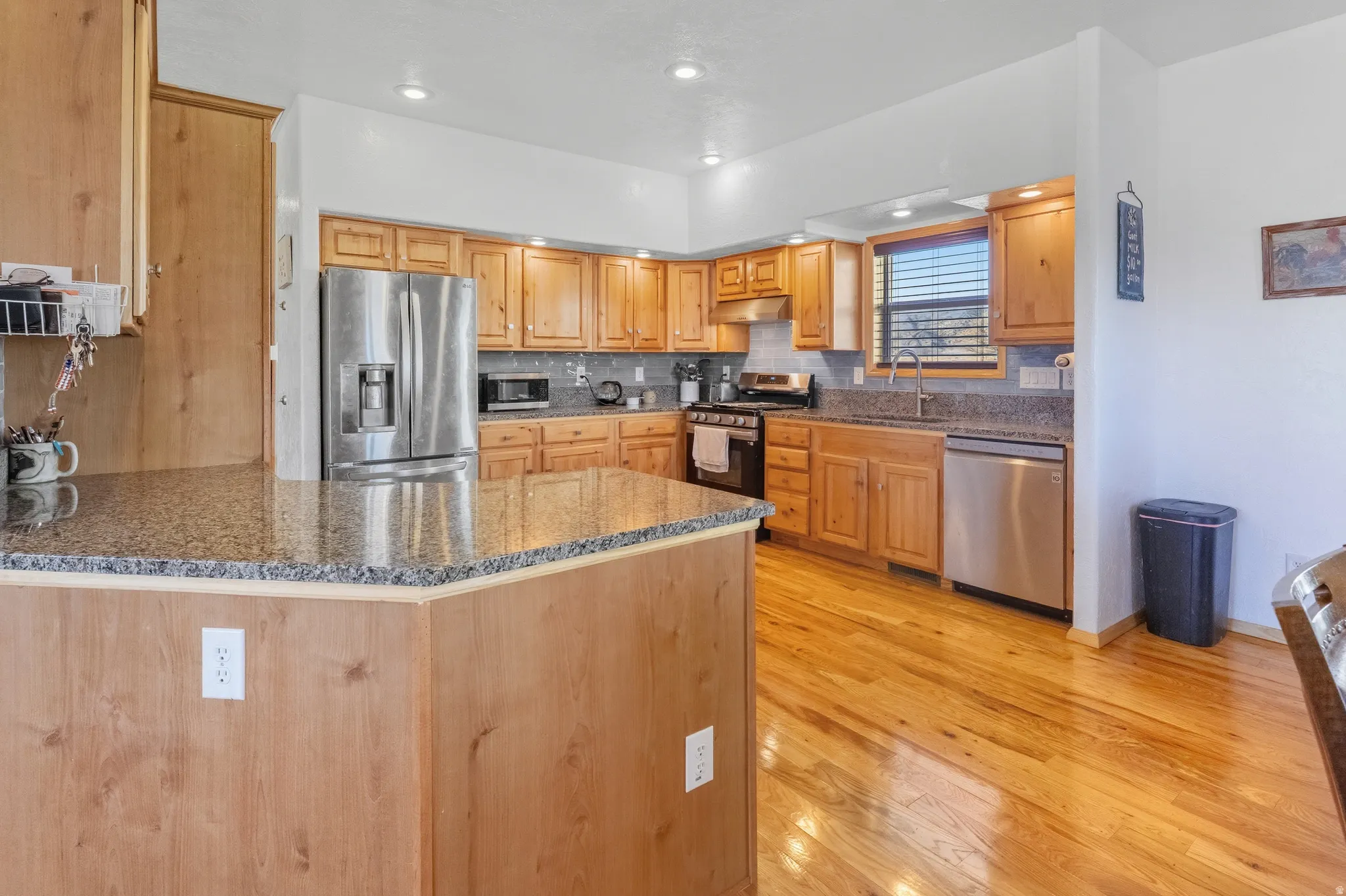 Kitchen featuring dark stone counters, stainless steel appliances, a peninsula, light wood-type flooring, and recessed lighting