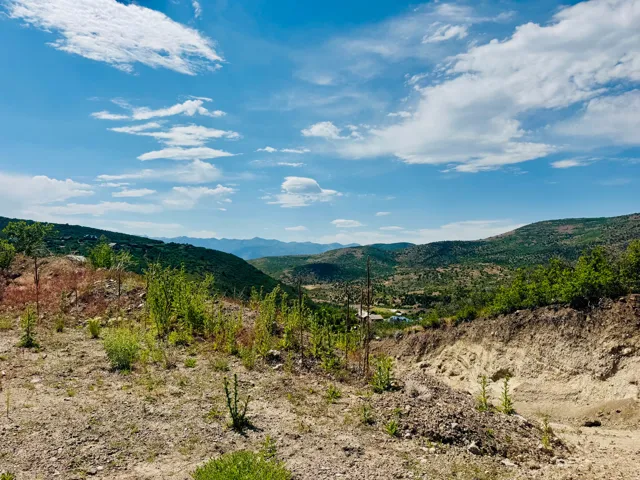 Expansive mountain landscape under a broad blue sky with scattered clouds