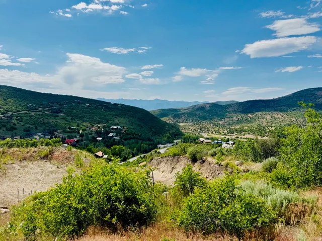 Expansive mountain landscape featuring a lush valley and distant peaks under a blue sky with scattered clouds