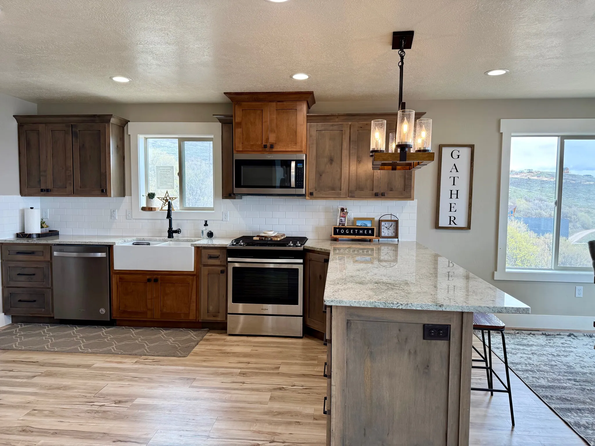 Kitchen featuring stainless steel appliances, a peninsula, a kitchen bar, light stone countertops, and hanging light fixtures