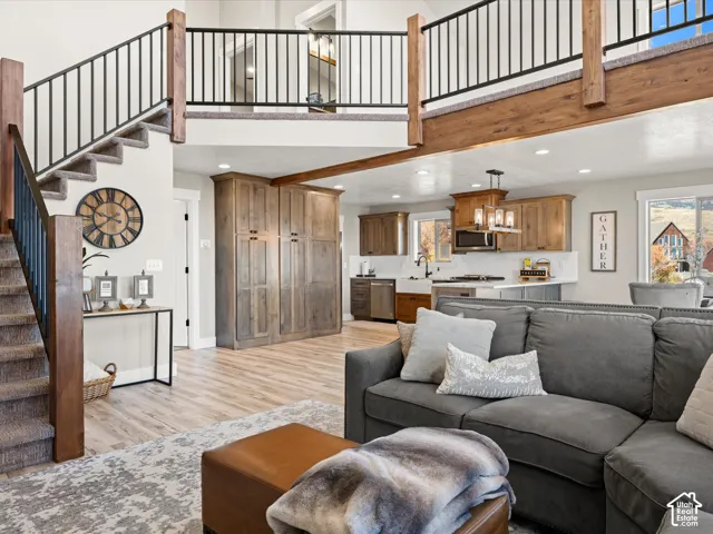 Open-concept living area featuring a kitchen with light wood-finish cabinetry, stainless steel appliances, and a farmhouse sink