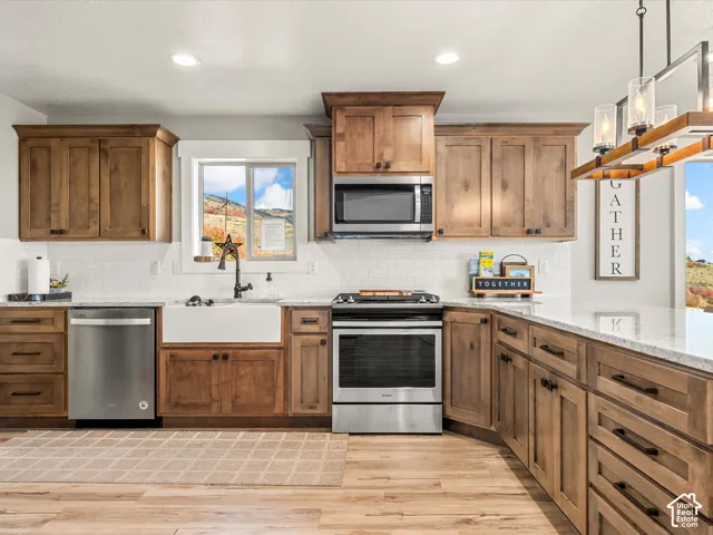 Kitchen featuring wood-finish cabinetry, stainless steel appliances, a farmhouse sink, subway tile backsplash, and light-toned countertops