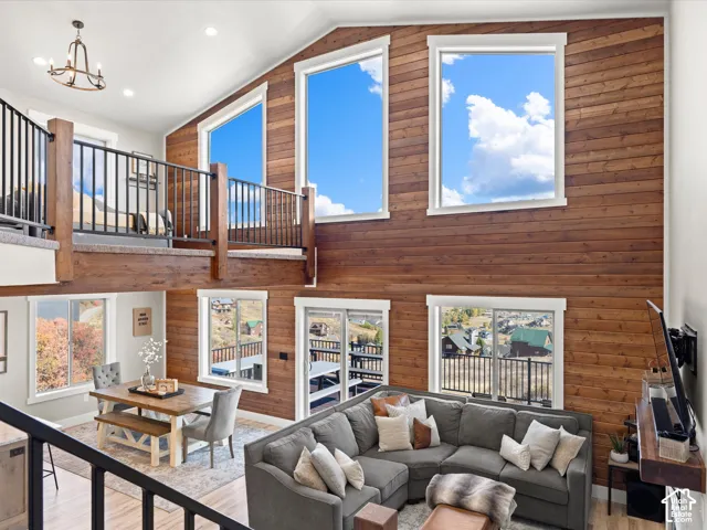 Vaulted ceilings with clerestory windows, wood-paneled accent wall, open-concept living area, upper-level balcony, and wood-finish flooring