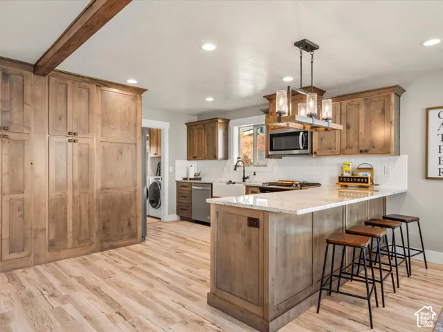 Kitchen featuring wood-finish flooring, custom wood cabinetry, a central island with a light-toned countertop, recessed lighting, and a white subway tile backsplash