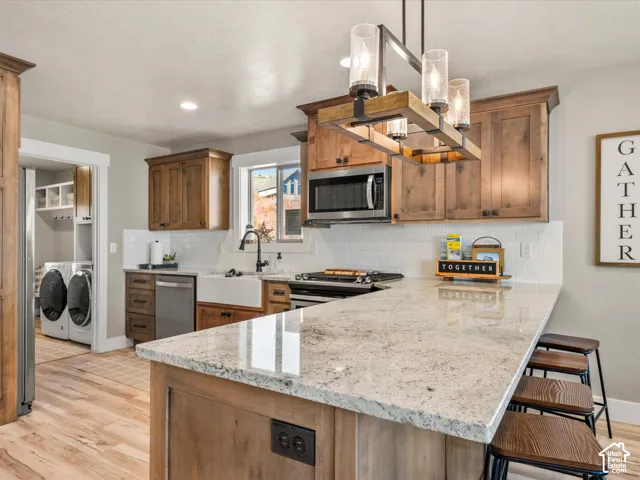 Kitchen featuring an expansive island with a light-toned countertop, wood-finish cabinetry, stainless steel appliances, a farmhouse sink, and a white subway tile backsplash