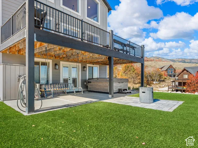 Ground-level concrete patio with an overhead deck, a paver patio area, and a hot tub
