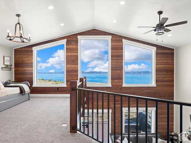Vaulted ceiling with recessed lighting, three large windows, wood-paneled accent wall, dark-finish ceiling fan, and a wood and metal railing