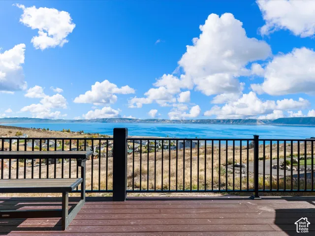 Expansive outdoor deck with wood-finish decking, black metal railing, and a broad water body in the background