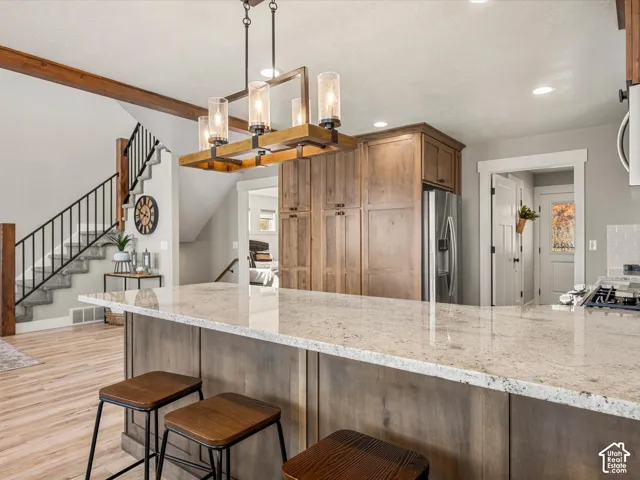 Kitchen island with light-toned countertop, wood-finish cabinetry, and stainless steel refrigerator