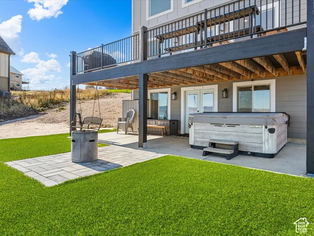 Expansive artificial turf, paver patio, concrete fire pit, double glass-paneled doors, and an integrated hot tub