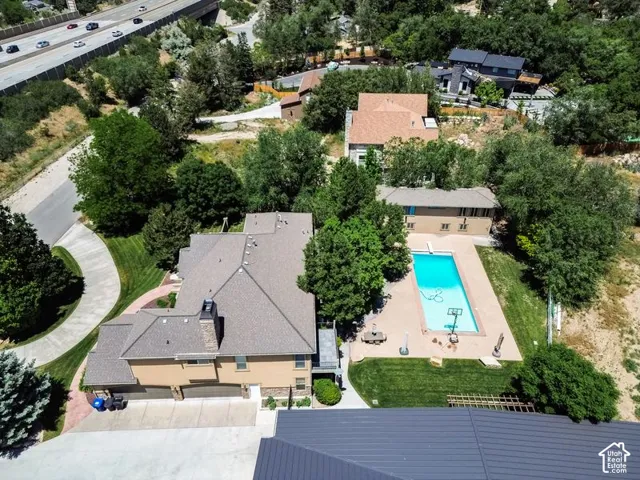 Aerial view showcasing a residential compound with a sparkling resort-style swimming pool, expansive manicured grounds with mature tree coverage, multi-structure layout with neutral-toned roofing, and proximity to major thoroughfare access