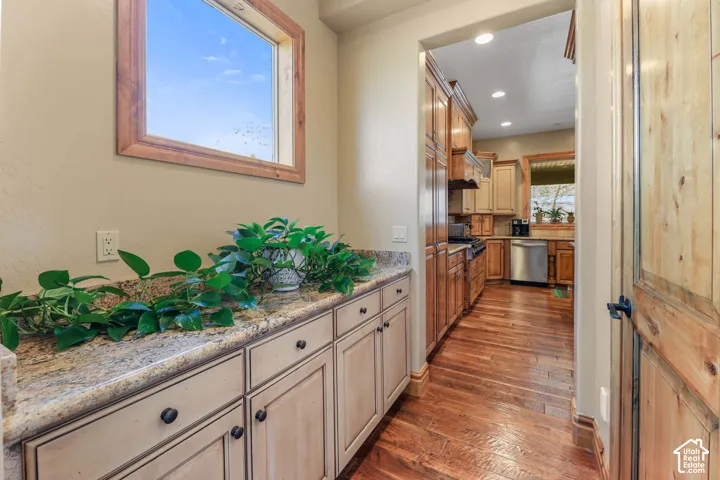 Kitchen featuring dark wood-type flooring, stainless steel dishwasher, light stone countertops, recessed lighting, and cream cabinetry
