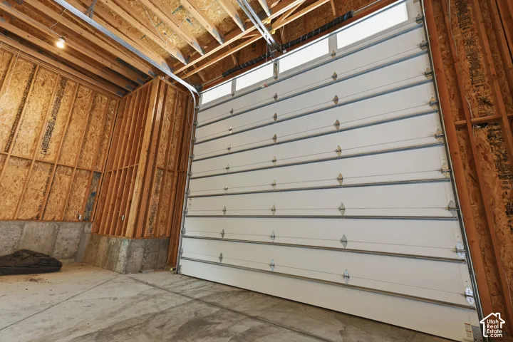 Interior framing and exposed rafters with a concrete floor and white sectional garage door with upper transom windows
