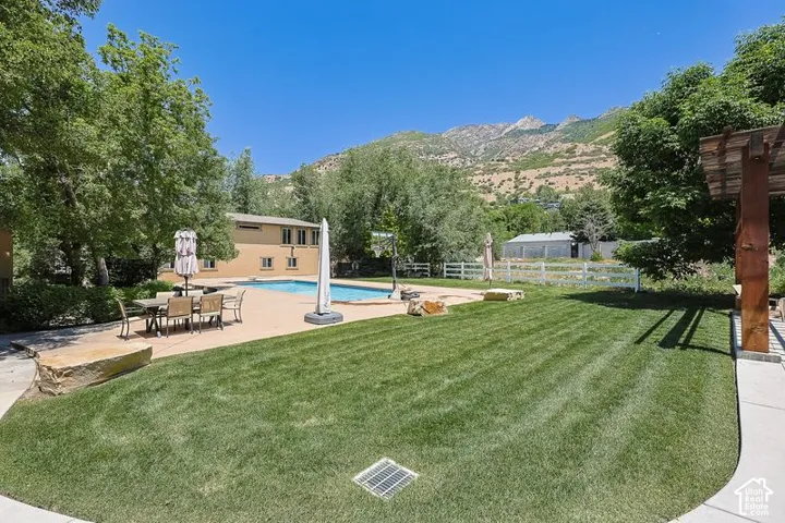 Expansive backyard oasis featuring a manicured lawn with professional striping, mature shade trees, resort-style saltwater pool with spa, dining patio with seating area, and mountain backdrop