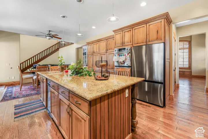 Kitchen with stainless steel appliances, wood finish cabinets, pendant lighting, light stone countertops, and light wood-type flooring