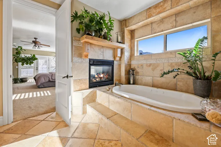 Full bathroom with stone tile floors, a bath, a fireplace, ensuite bath, and healthy amount of natural light