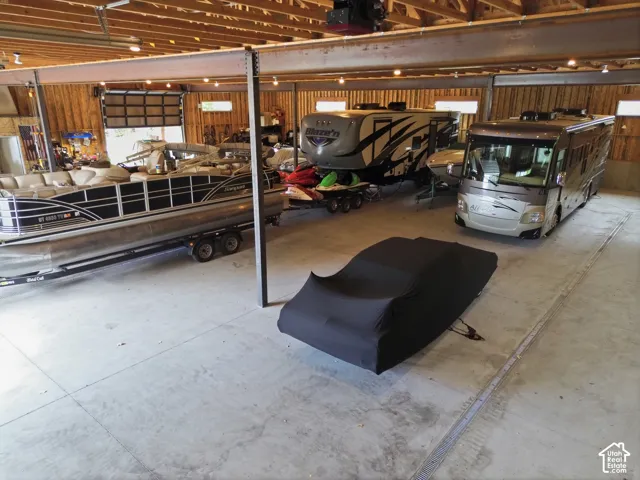 Spacious storage facility featuring exposed wood beam ceiling, concrete flooring, overhead lighting, and two large garage doors