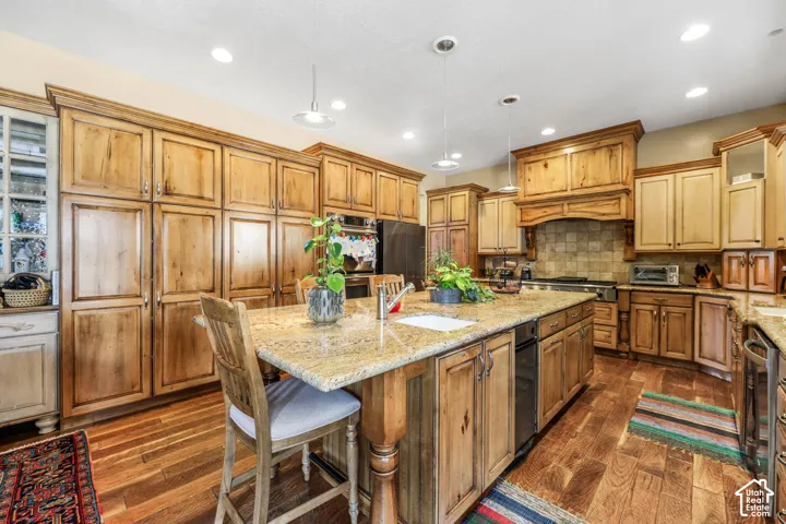 Kitchen with a breakfast bar, light stone countertops, an island with sink, pendant lighting, and wood finish cabinets