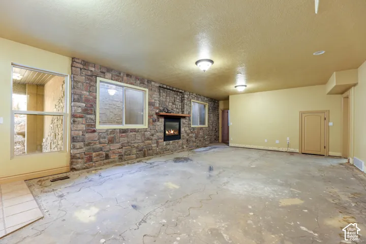 Unfurnished family room featuring a brick fireplace, a textured ceiling, an accent wall, and concrete floors