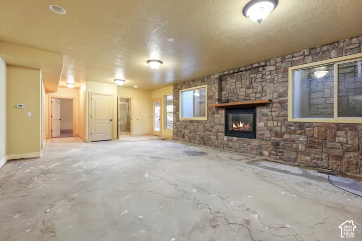 Unfurnished family room with a textured ceiling, concrete flooring, and a large fireplace
