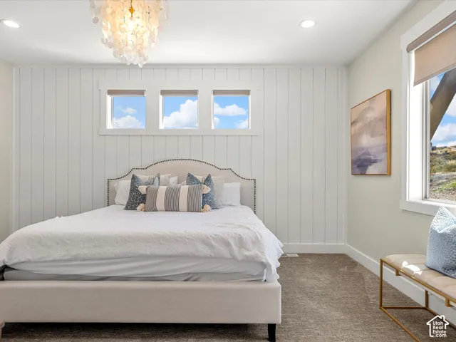 White shiplap accent wall, upholstered bed frame with nailhead trim, three transom windows, recessed lighting, and a decorative chandelier