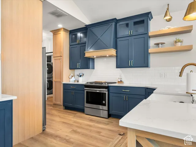 Navy cabinetry with gold-tone hardware, stainless steel range, white subway tile backsplash, light wood-finish flooring, and white countertops