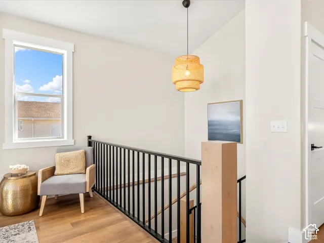 Wood-finish flooring, white trim windows, black iron balusters, light wood newel post, and a decorative pendant light fixture