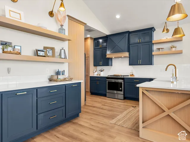 Wood-finish flooring, white subway tile backsplash, white countertops, and blue shaker-style cabinetry with gold-tone hardware