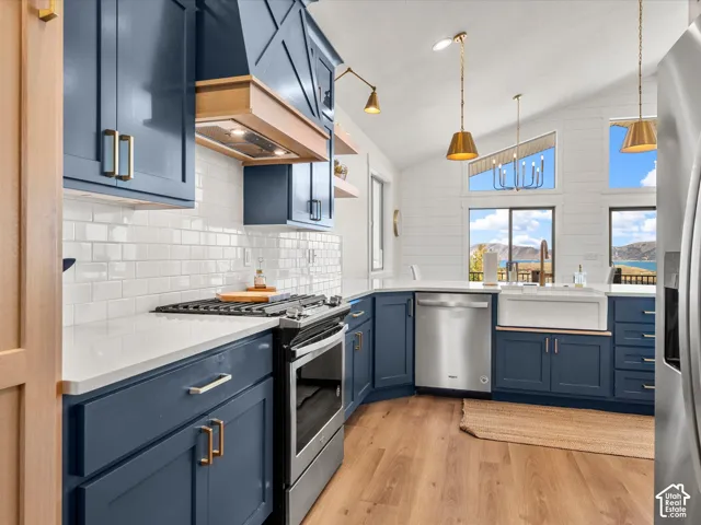 Kitchen featuring vaulted ceilings, wood-finish flooring, white subway tile backsplash, blue cabinetry, and stainless steel appliances