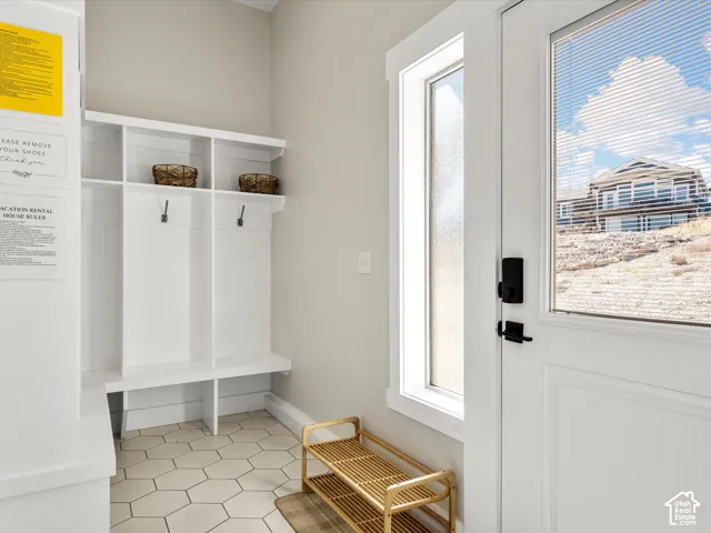 Built-in storage bench with overhead shelving and coat hooks, hexagonal floor tiling, and a white entry door with frosted glass and a smart lock