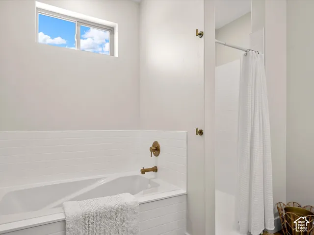 Soaking tub with brass fixtures, separate shower,  white subway tile surround, and an upper transom window
