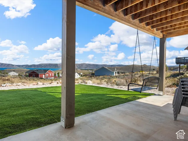 Concrete patio with a wooden beam structure and a suspended porch swing, featuring a manicured artificial turf lawn