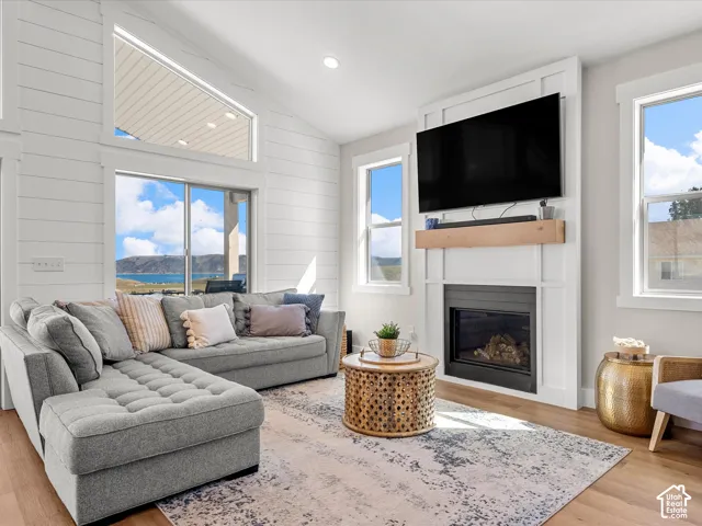 Vaulted ceilings, wood-finish flooring, white shiplap accent wall, built-in fireplace, and expansive windows