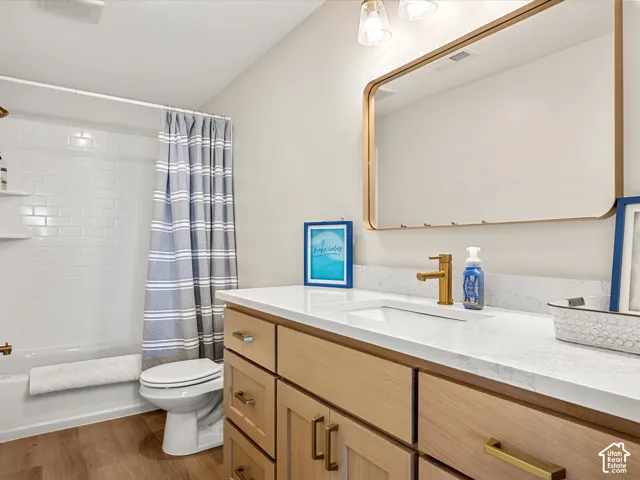 Wood-finish flooring, light wood cabinetry, white countertop, rectangular undermount sink, and a gold-framed mirror