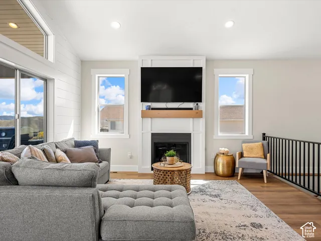 Vaulted ceiling with recessed lighting, shiplap accent wall, fireplace with white mantel and wood-finish hearth, wood-finish flooring, and black metal railing